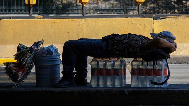Vendedor ambulante descansa a la sombra sobre paquetes de botellas